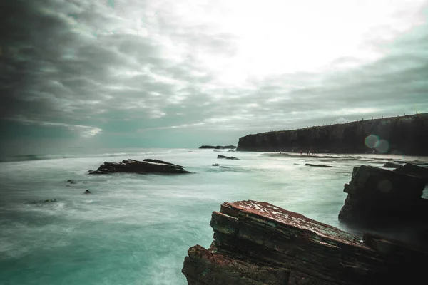 日の出には曇りの空に対して嵐の海の岩の海岸 — ストック写真
