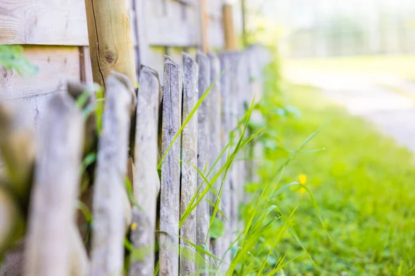 A closeup of wooden fence and grass by the road on a sunny day