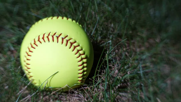 A yellow softball in the grass with copy space on the side