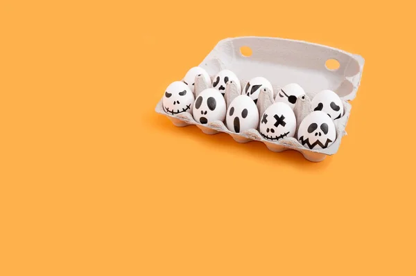 A egg carton of many eggs with faces and emotions drawn on them on an orange table