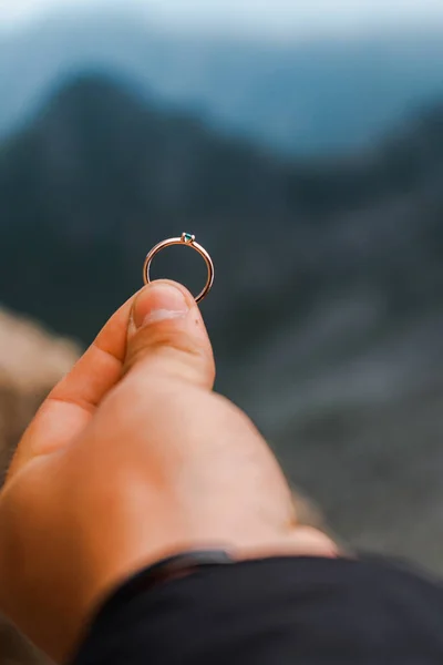 青い山のぼんやりとした背景に提案のための婚約指輪を持っている男の手の閉鎖 — ストック写真