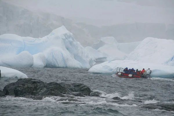 南極の冷たい水の中の小さな船に氷の塊で航海する人々のグループ — ストック写真