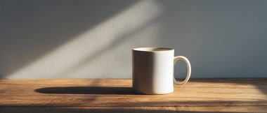 Temiz beyaz bir kupa, ahşap bir yüzeyde, yumuşak, rahatlatıcı gölgeler ve atmosfer yaratan, doğal güneş ışığıyla aydınlatılmış, zarif bir şekilde oturmaktadır..