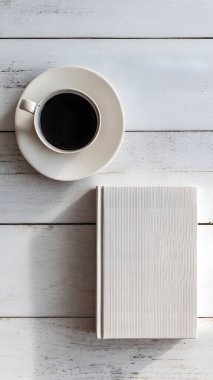 Ahşap bir yüzeyde bir fincan sütlü çayın yanında boş bir kitabın yer aldığı samimi bir sabah sahnesi..