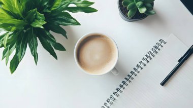 Boş bir defter ve taze yeşilliklerle çevrili sade bir kahvenin verimli bir sabah başlangıcı olduğu temiz bir çalışma alanı..