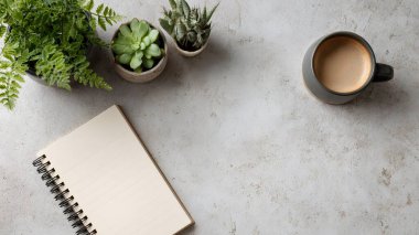 Boş bir defter ve taze yeşilliklerle çevrili sade bir kahvenin verimli bir sabah başlangıcı olduğu temiz bir çalışma alanı..