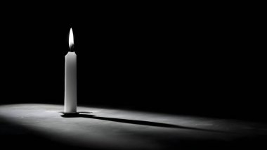 Yalnız beyaz bir mum, koyu bir arka planda parlar, dokulu bir yüzeye uzun ve dramatik bir gölge bırakır..