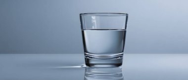 Temiz suyla dolu berrak bir bardak gri dokulu bir duvara yaslanmış, temiz ve minimalist bir estetik yaratıyor..