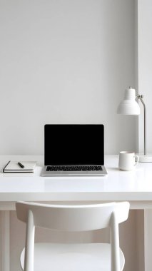 Temiz profesyonel bir masa parlak beyaz bir odada dizüstü bilgisayar içerir. Odaklanmış yaratıcı işler için mükemmel bir atmosfer yaratır..