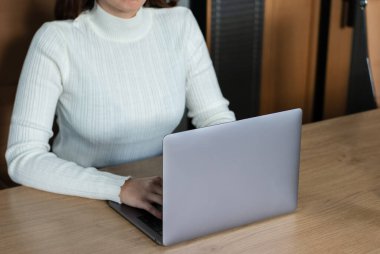 Beyaz kazaklı kadın ofiste dizüstü bilgisayarla çalışıyor.