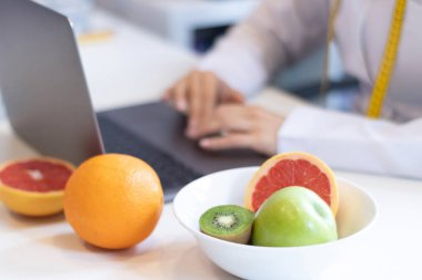 Bilgisayarıyla çalışan dietisyen kadın ve masada karışık meyve ve su olan bir ofis.