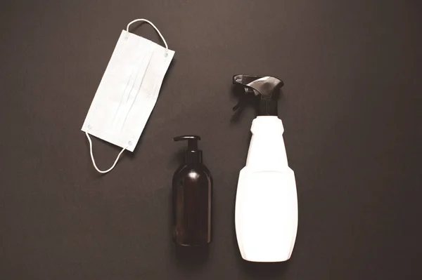 Hygiene and cleaning products: medical protective masks, bottle of antiseptic and liquid soap over black background close up. Top view.