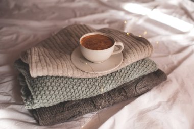 Bir fincan köpüklü kahve örülmüş süveter yığınının üzerinde duruyor. İyi sabahlar. Kahvaltı vakti geldi. Kış mevsimi.