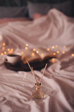 Sıvı ev parfümü cam şişede. Evdeki yatakta parlayan ışıkların üzerinde çubuklar var. Sıcak atmosfer konsepti. Tazelik.