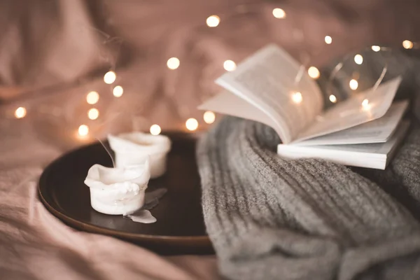在木制盘子里放上蜡烛 配上针织毛衣 在床上的灯火通明的地方翻开纸质书 寒假季节 圣诞节 温暖舒适的家庭氛围 免版税图库照片