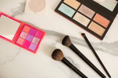 Makyaj ürünleri: pembe gölgeli göz gölgeleri ve mermer masa üzerinde fırçalar. Üst görünüm.