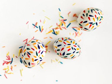 Paskalya yumurtaları kırmızı, sarı, mavi boyalarla boyanır beyaz arka planda, üzerine renkli çubuklar serpiştirilir.