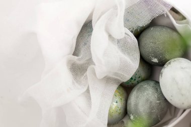 Yeşil ve altın lekeli gri ve beyaz renkte Paskalya yumurtaları. Yuvarlak bir kutunun içindeki yumurtalar açık beyaz bir raptiye ile kaplıdır..