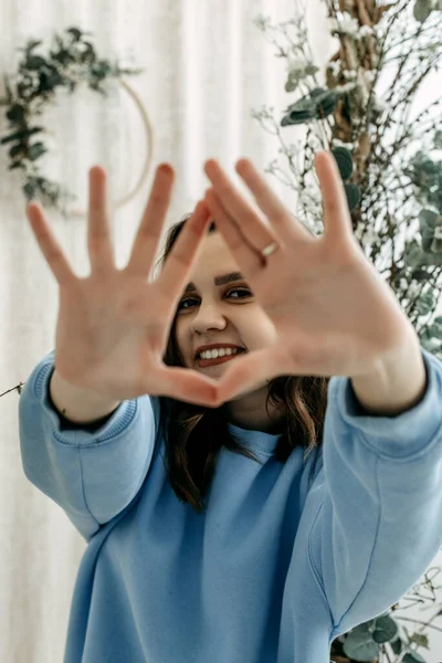 The brunette stretched out her arms in front, folding her fingers in a triangle and looking through them. Hands out of focus. The face of a pretty brunette in a blue sweater through the palms.