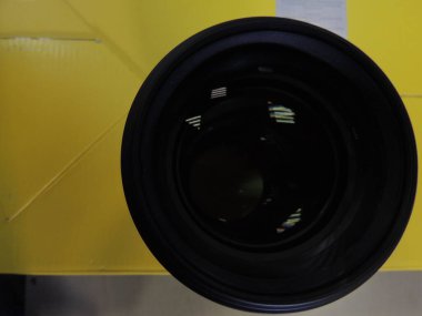 Genç bir adamın erkek elinde mercek yansıması olan kamera merceği. Karanlık arka plan. Kolunda bilezik var. Renkli gölgeler ve yansımalar. Makro. Cam ve yansıma.