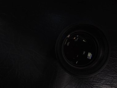 Genç bir adamın erkek elinde mercek yansıması olan kamera merceği. Karanlık arka plan. Kolunda bilezik var. Renkli gölgeler ve yansımalar. Makro. Cam ve yansıma.