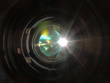 Genç bir adamın erkek elinde mercek yansıması olan kamera merceği. Karanlık arka plan. Kolunda bilezik var. Renkli gölgeler ve yansımalar. Makro. Cam ve yansıma.