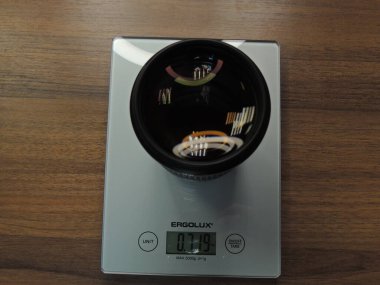Elektronik ölçeklerde kamera lensi. Lensi tartıyorum. Ahşap arka plan. Koyu renk. Gümüş renkli elektronik pullar..