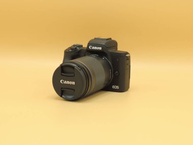 Sarı arka planda EF-M 18-150mm f3.5-6.3 lens ile Canon EOS M50 mark ii (M50m2). Blogcular için en iyi kameralardan biri..