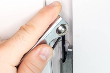 Plastik PVC penceresinin konfigürasyonu ve bakımı. Bir adam evdeki plastik pencereyi ayarlıyor. Kilit mekanizmasının altıgen anahtarla ayarlanması.