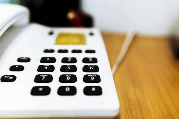 Masanın üzerinde siyah düğmeler olan klasik itme düğmeli beyaz telefon, bulanık