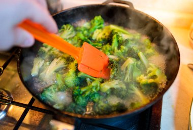 Brokoli, dökme demir tavada turuncu bir spatulayla karıştırılır.