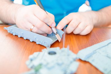 Bir adam plastikten oyuncak tankın modelini toplar, plastik bıçakla burrları temizler.