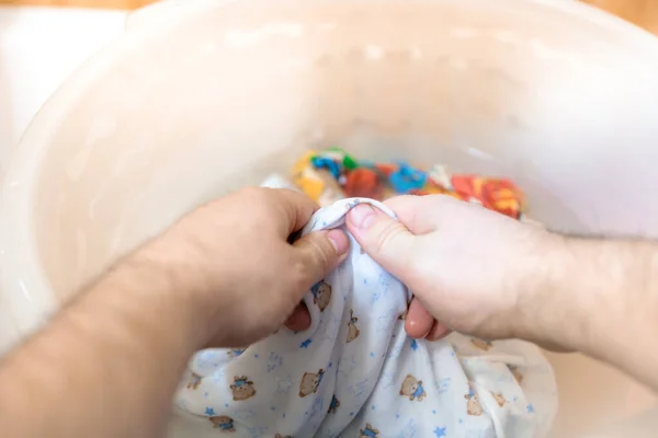 Bir adam bebek kıyafetlerini havuzda elleriyle yıkıyor.