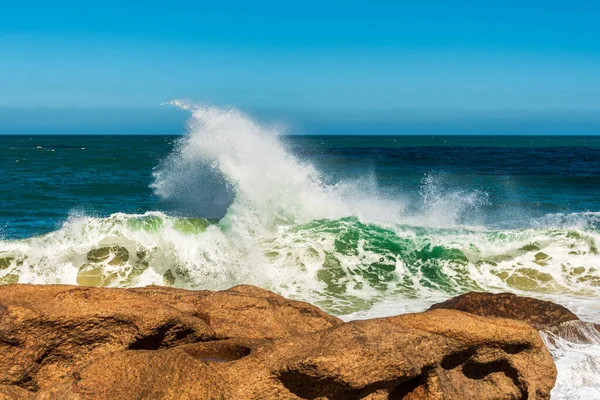 Green wave splashing white foam when crashing against rocks in the sea