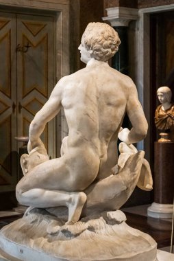 Çıplak bir adamın oturduğu mermer heykelin arkasında.
