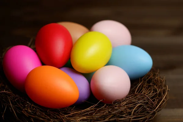 Multi colored easter eggs in birds nest on dark wooden planks table closeup view selective focus. Easter celebration. Easter holiday banner, card, poster, voucher, invitation templat