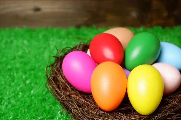 Multi colored easter eggs in birds nest on green grass and wooden panks background closeup view selective focus with copy space. Easter holiday banner, card, poster, voucher, invitation templat
