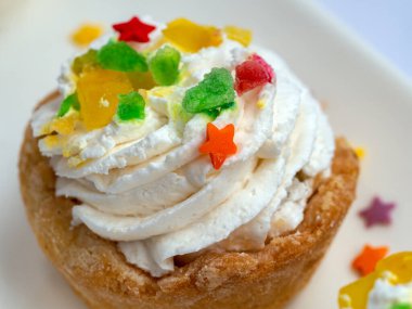 Kremalı hamur işi sepeti. Yakın plan. Krema spiral şeklinde serilmiş. Üstte, renkli ve şekilli şekerlemeler var. Pastalı yemek arkaplanı.