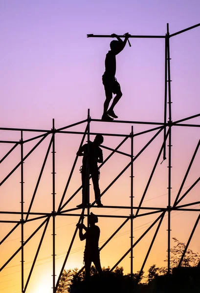 Silhouettes of workers against the sunset sky. Workers stand at different heights of the metal structure and dismantle the frame.