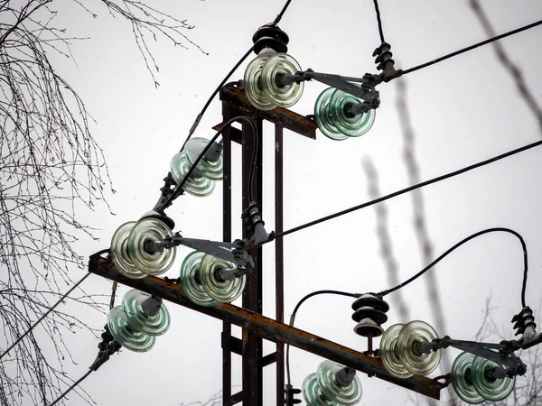 Insulators made of durable glass are attached to the metal pole of the power line. Wires are attached to insulators, through which current flows. Insulators and wires close up.