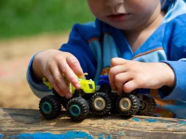 Küçük bir çocuk elinde mavi ve sarı oyuncak bir araba tutuyor. Bir çocuk yalan kütüğünde birbirine doğru giden arabaları yuvarlıyor. Oyuncak arabalarla çocuk oyunu.