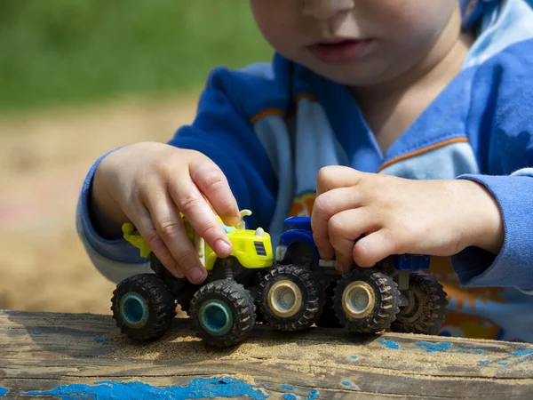 Küçük bir çocuk elinde mavi ve sarı oyuncak bir araba tutuyor. Bir çocuk yalan kütüğünde birbirine doğru giden arabaları yuvarlıyor. Oyuncak arabalarla çocuk oyunu.