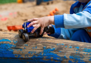 Bir çocuğun eli oyuncak bir arabayı tutar ve kütüğe yuvarlar. Çocuk kum havuzunda oynuyor. Renkli arkaplan.
