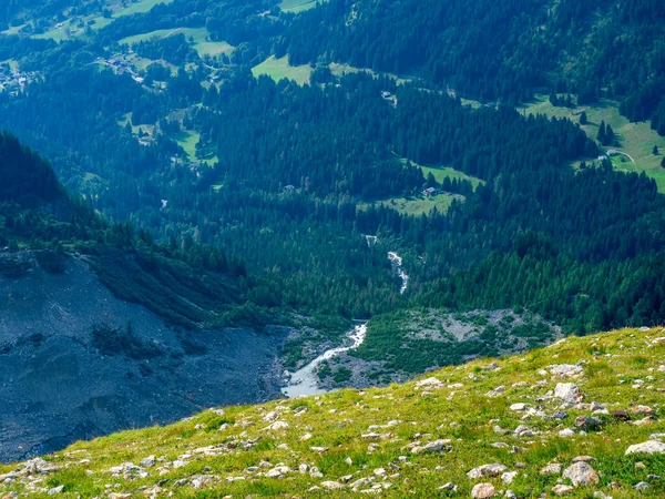 Çimenli yamaçta birçok taş var. Yokuştan ormanları, tarlaları, bir nehri ve küçük evleri görebilirsiniz. Doğal dağ manzarası. Yukarıdan görüntüle.