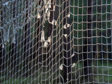 Futbol gollerinin eski yırtık pırtık ağı güneş tarafından aydınlatılıyor. İp ağ arkaplanı.