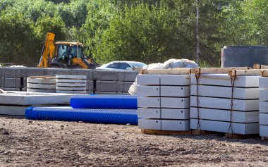 Reinforced concrete blocks, well rings, corrugated plastic pipes are stacked at the construction site. A tractor is visible behind them. Building materials for the improvement of the city.