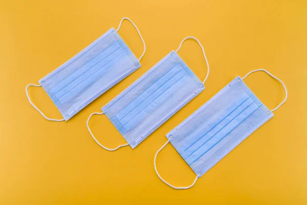 three surgical mask as blue covid 19 coronavirus protection isolated on saturated yellow background. Top view