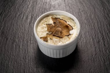 Fırınlanmış yumurta ve dilimlenmiş fontina peynirli fondü. Siyah kayrak taşı yüzeyinde dilimlenmiş mantarlı mantar.