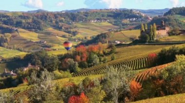 Barolo, Alba, Langhe, Piedmont, İtalya 'da sonbahar renklerinde üzüm bağlarıyla tepelerin üzerinde uçan renkli sıcak hava balonu.