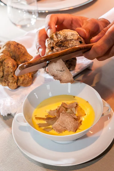 Alba white truffle sliced by the waiter\'s hands on fontina cheese fondue in a white elegant ceramic cup with two handles on the saucer, close up